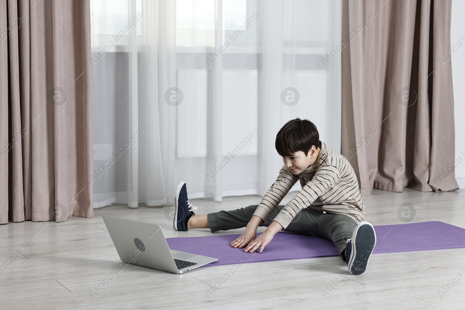 Photo of Little boy exercising near laptop at home. Morning routine