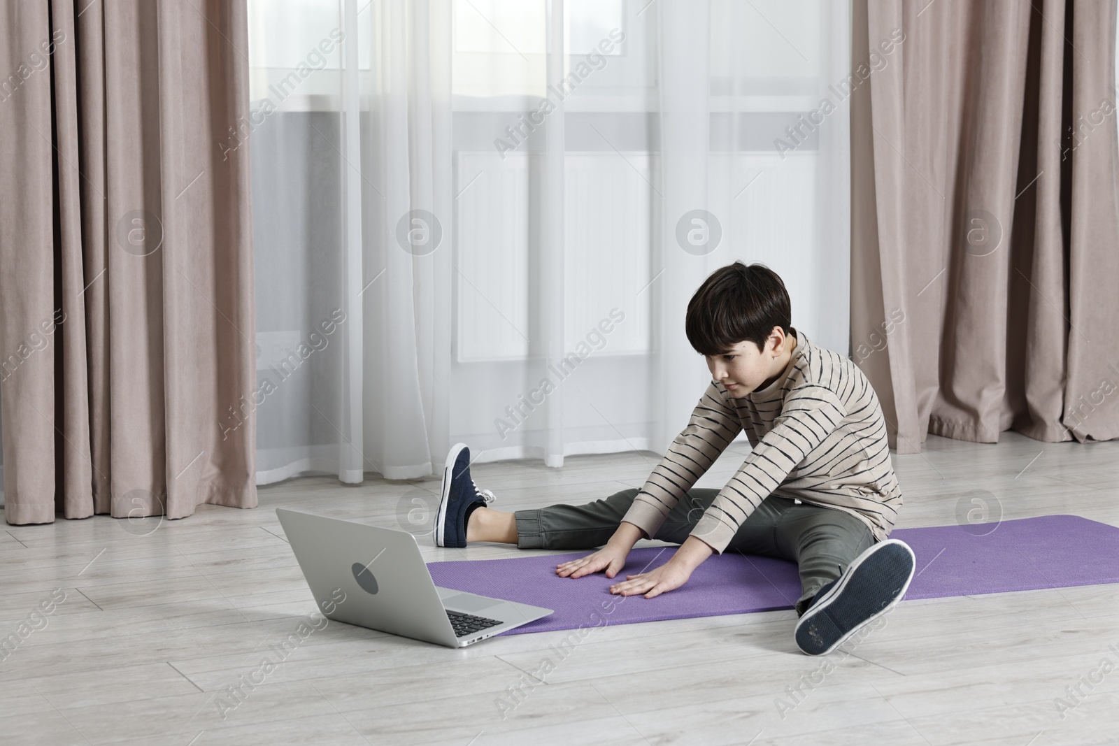 Photo of Little boy exercising near laptop at home. Morning routine