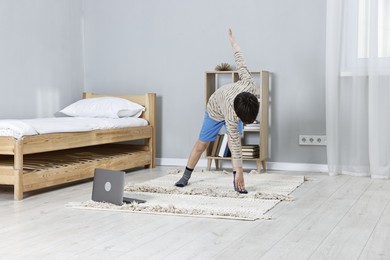 Photo of Little boy exercising near laptop at home. Morning routine