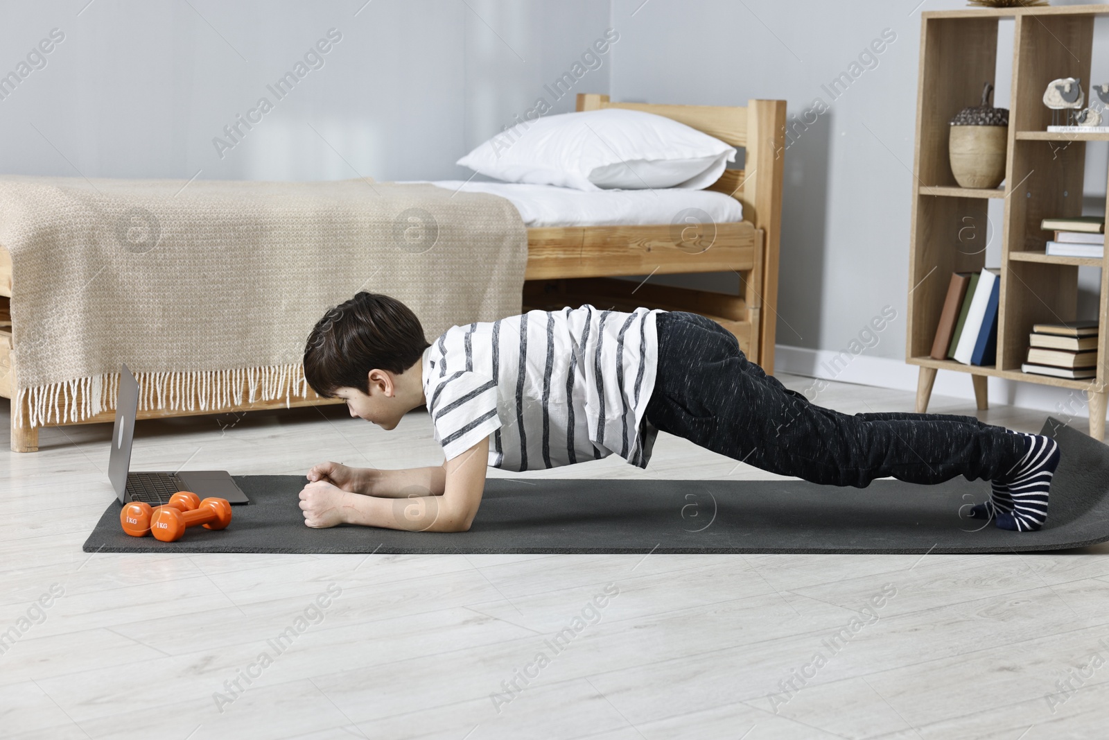 Photo of Little boy doing plank exercise near laptop at home. Morning routine