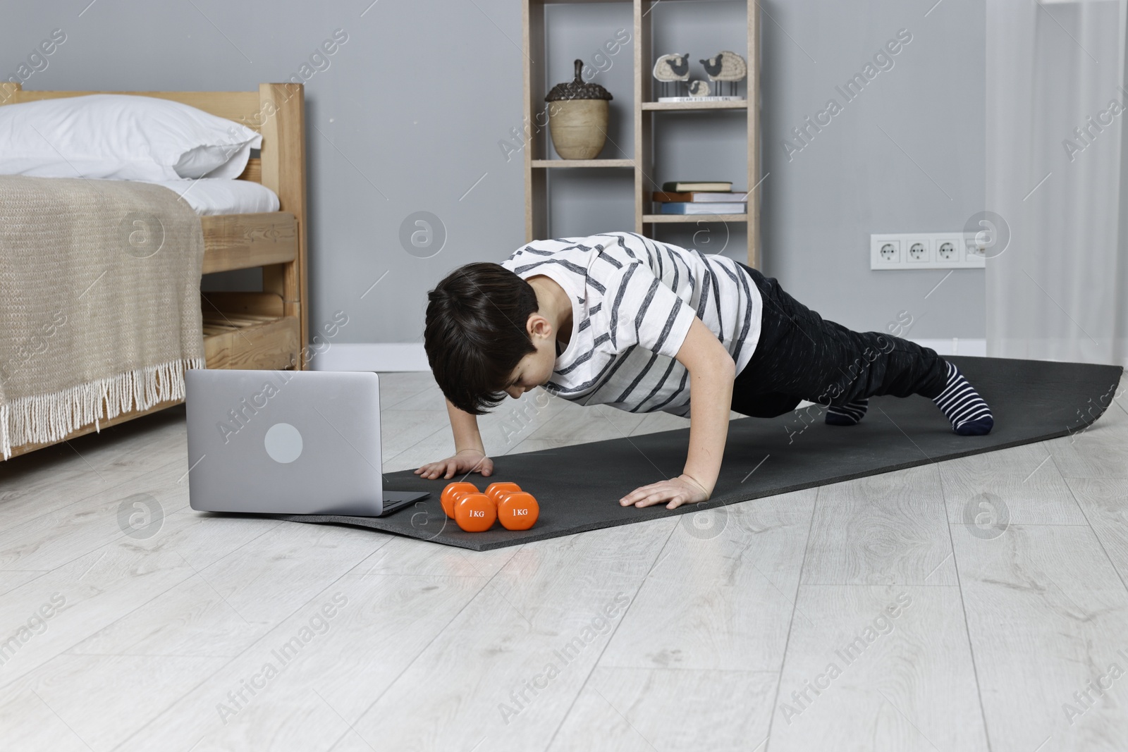 Photo of Little boy doing plank exercise near laptop at home. Morning routine