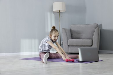 Photo of Little girl exercising near laptop at home, space for text. Morning routine