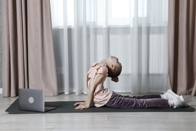 Photo of Little girl exercising near laptop at home. Morning routine