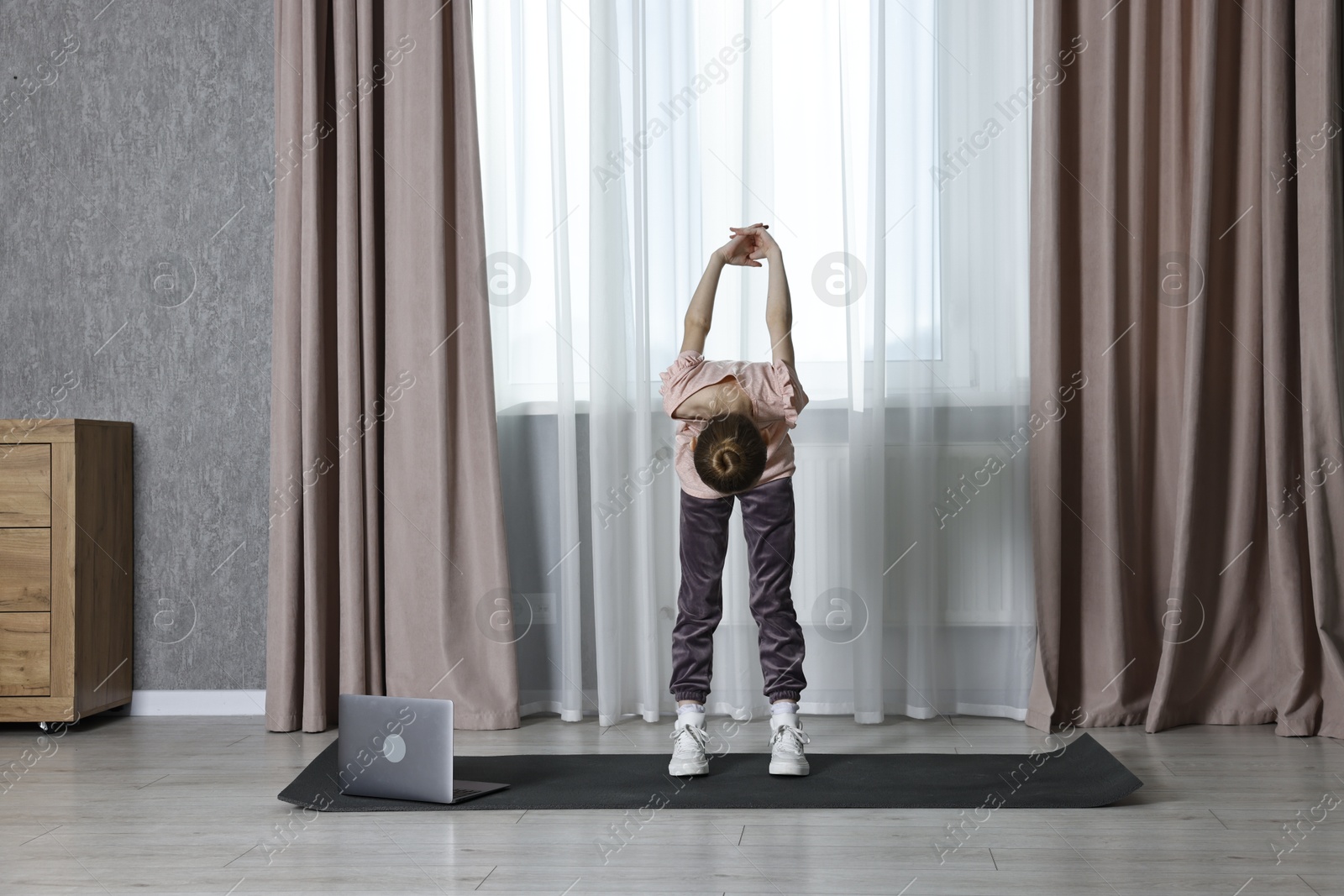 Photo of Little girl exercising near laptop at home. Morning routine