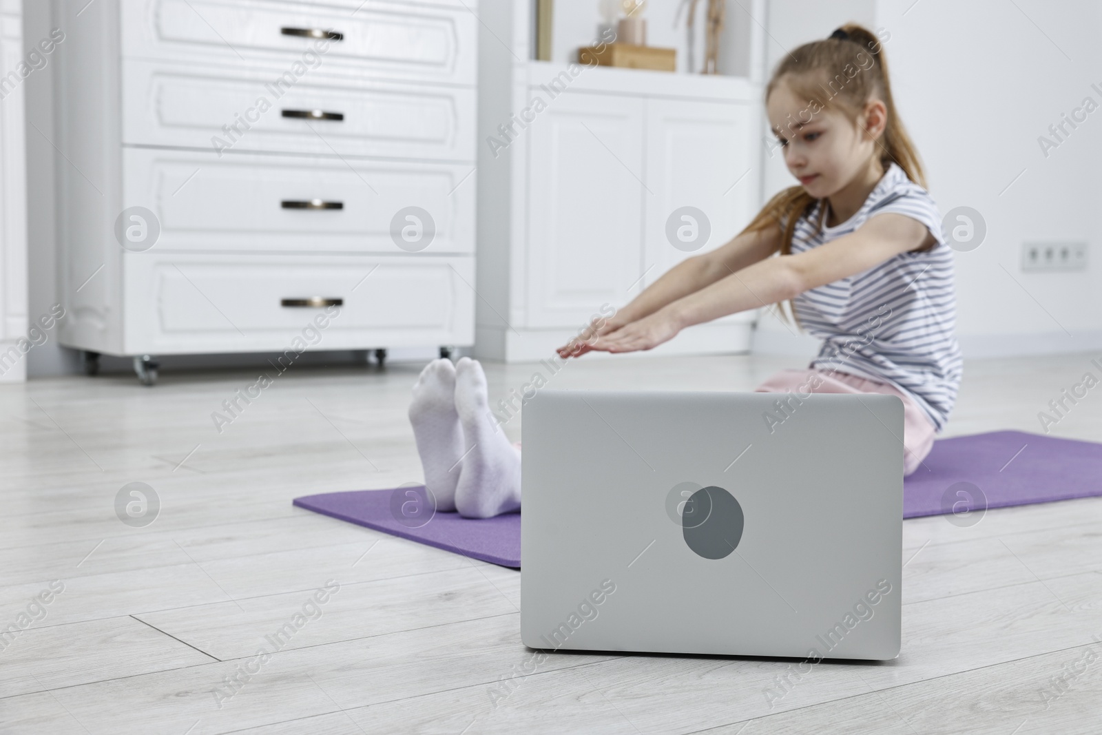 Photo of Little girl exercising near laptop at home, selective focus. Morning routine