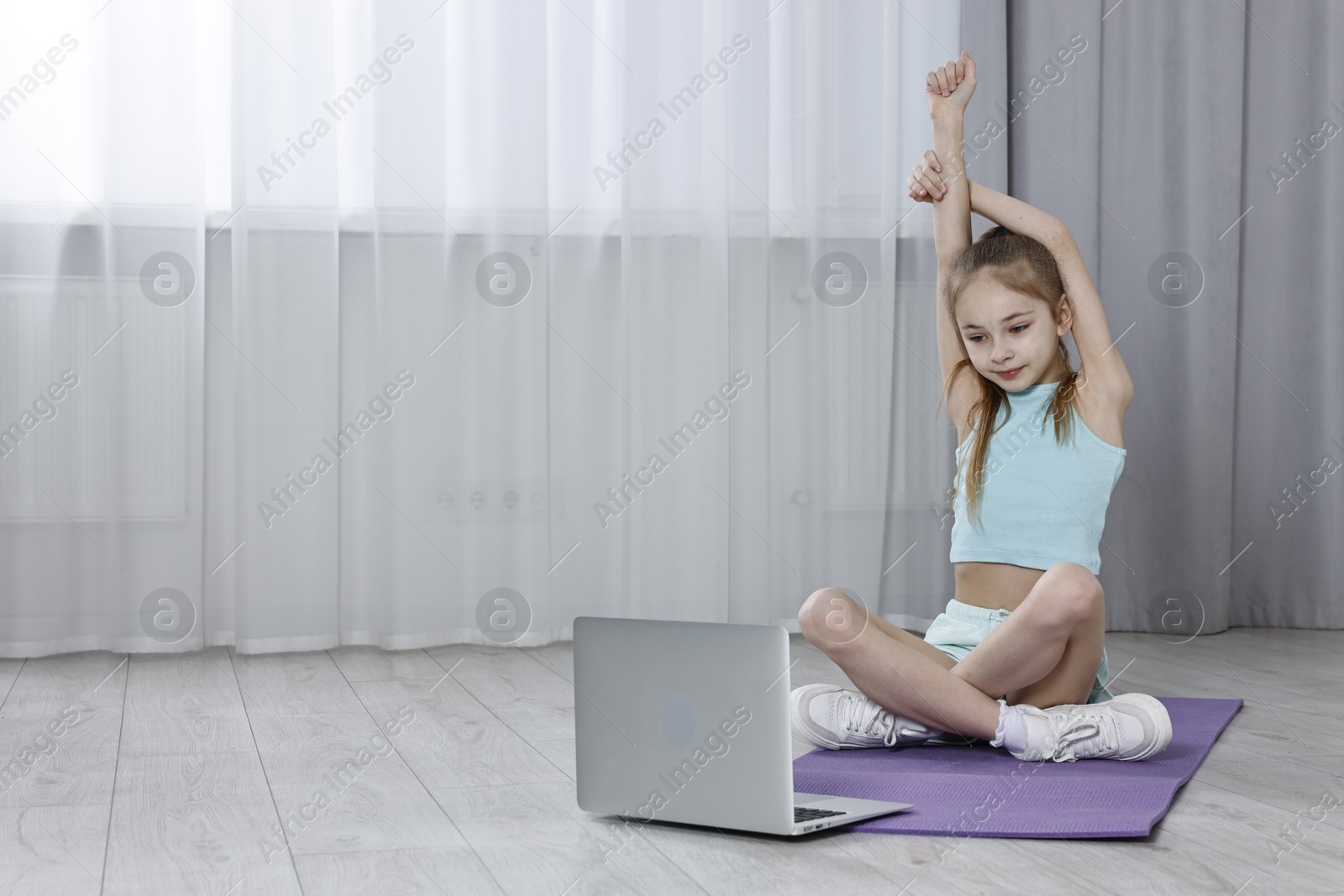 Photo of Little girl exercising near laptop at home, space for text. Morning routine