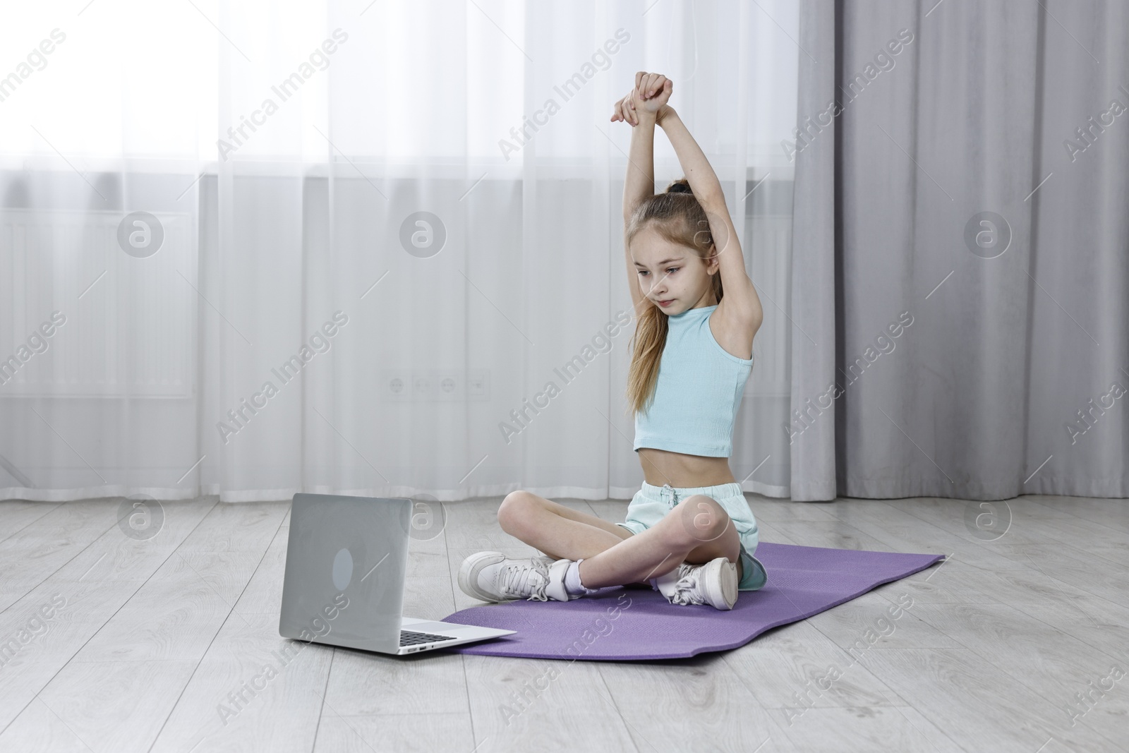 Photo of Little girl exercising near laptop at home, space for text. Morning routine