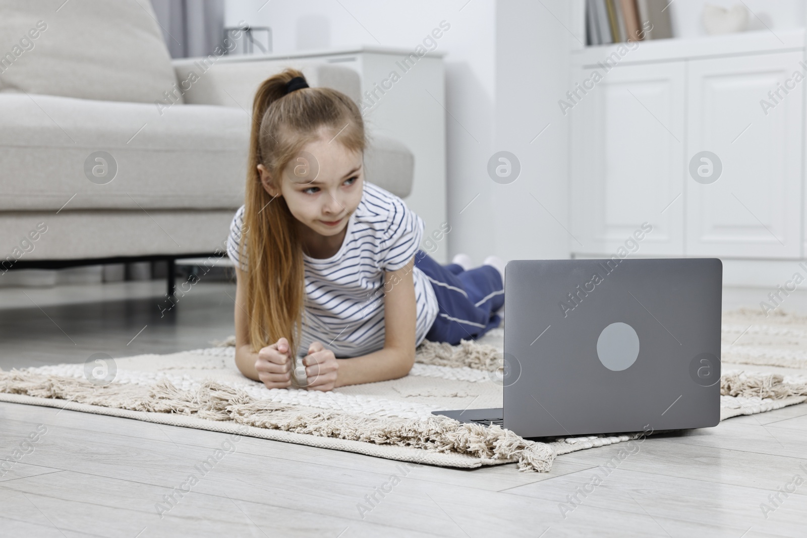 Photo of Little girl doing plank exercise near laptop at home. Morning routine