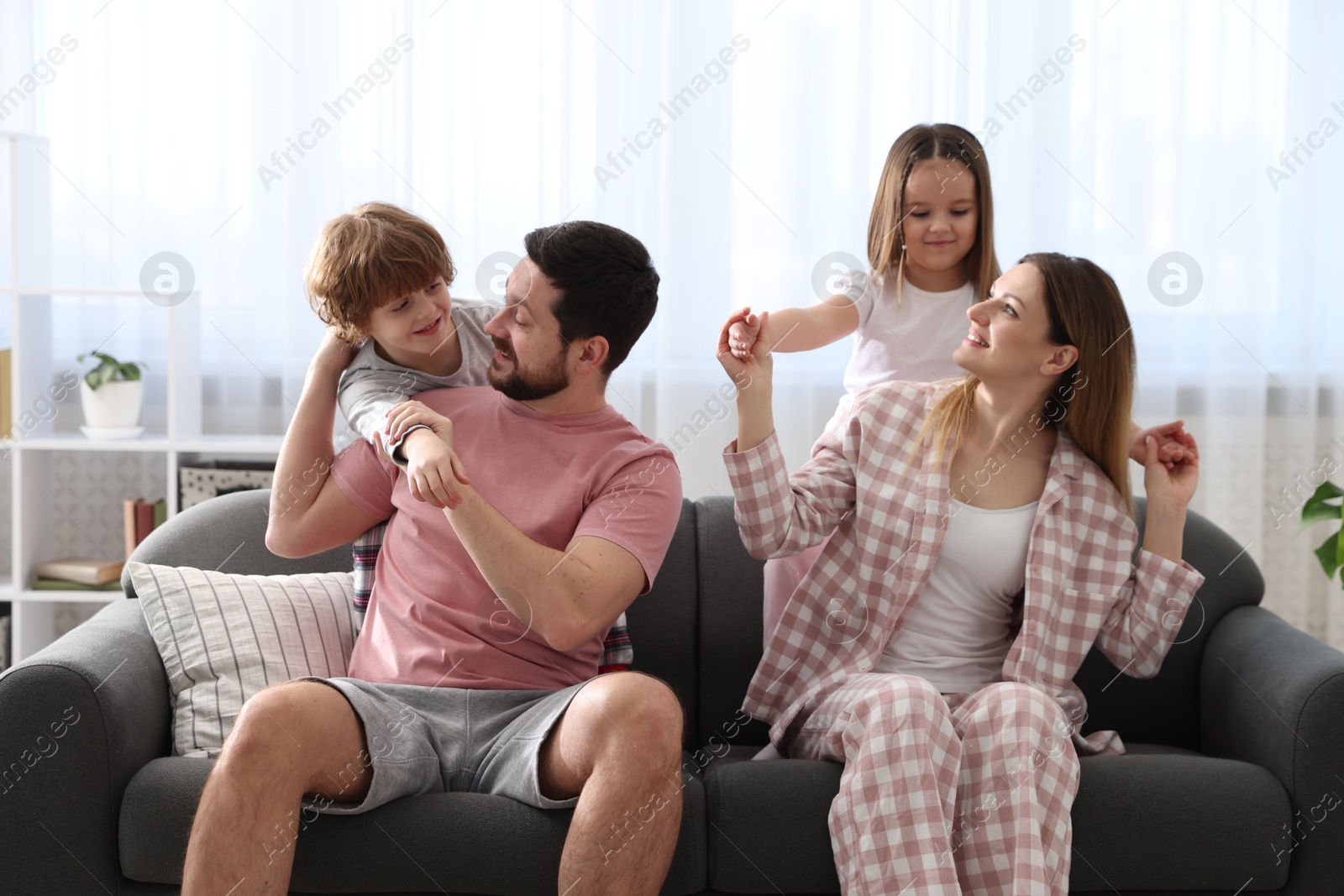 Photo of Happy family wearing stylish pajamas having fun on sofa at home