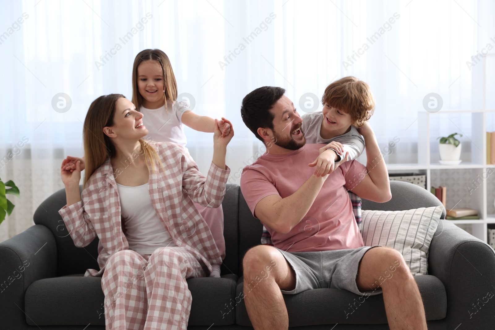 Photo of Happy family wearing stylish pajamas having fun on sofa at home