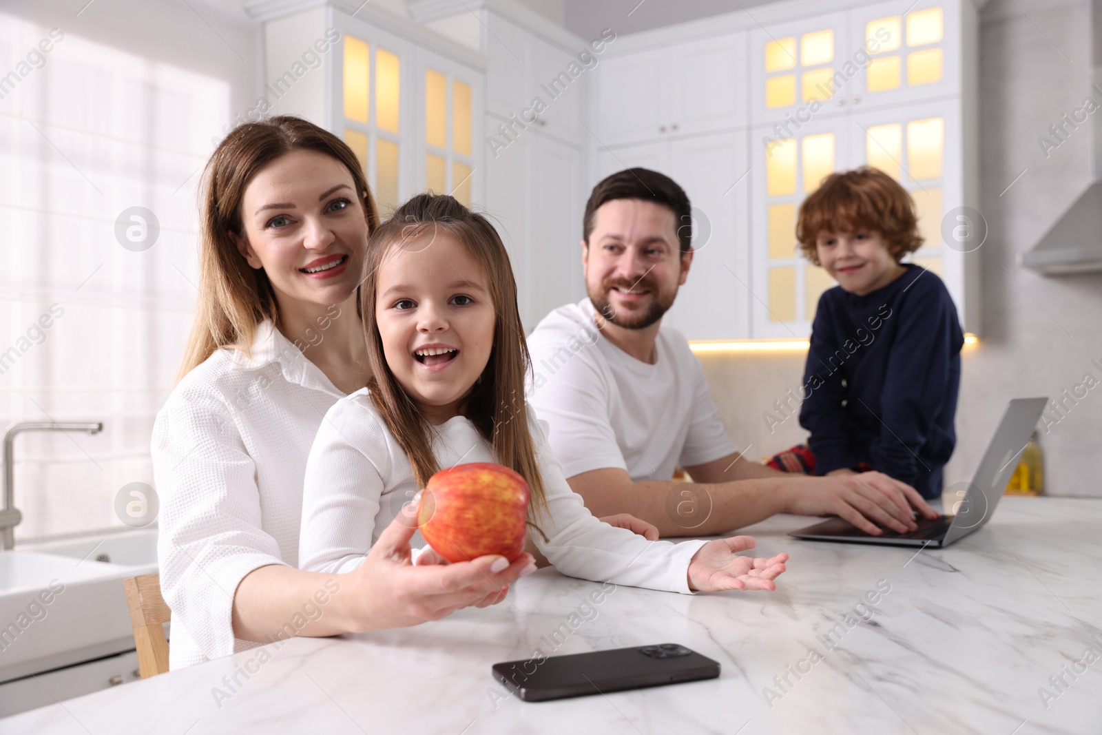 Photo of Happy family in stylish pajamas spending time together at white marble table in kitchen