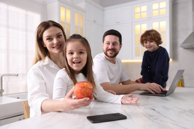 Photo of Happy family in stylish pajamas spending time together at white marble table in kitchen