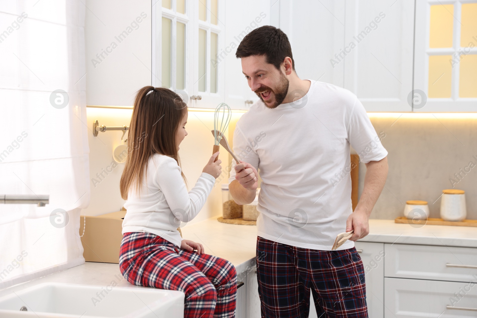 Photo of Happy father and his daughter wearing stylish pajamas playing with cookware in kitchen