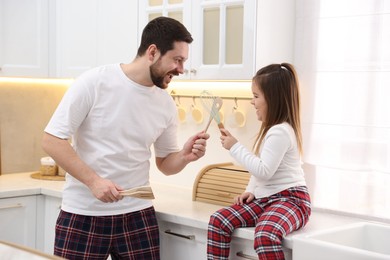 Photo of Happy father and his daughter wearing stylish pajamas playing with cookware in kitchen