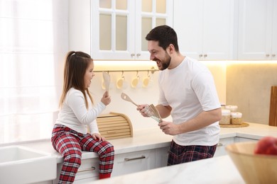 Photo of Happy father and his daughter wearing stylish pajamas playing with cookware in kitchen