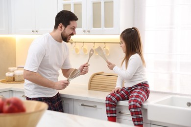 Photo of Happy father and his daughter wearing stylish pajamas playing with cookware in kitchen