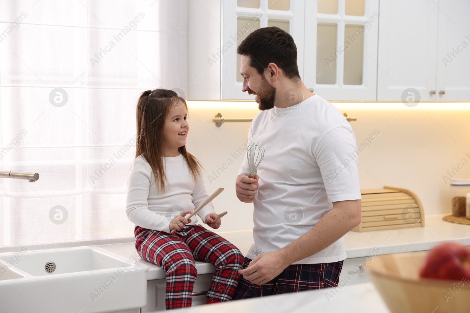 Photo of Happy father and his daughter wearing stylish pajamas having fun with cookware in kitchen