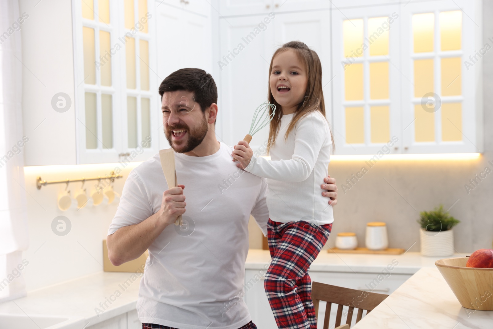 Photo of Father and his daughter wearing stylish pajamas having fun with cookware in kitchen