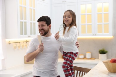 Photo of Father and his daughter wearing stylish pajamas having fun with cookware in kitchen