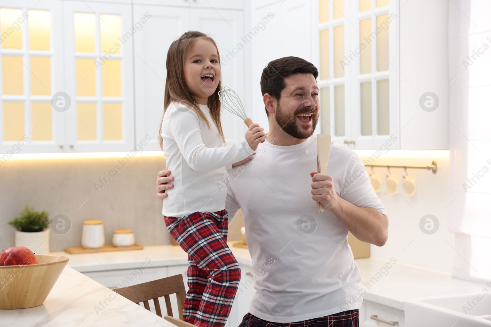 Photo of Father and his daughter wearing stylish pajamas having fun with cookware in kitchen