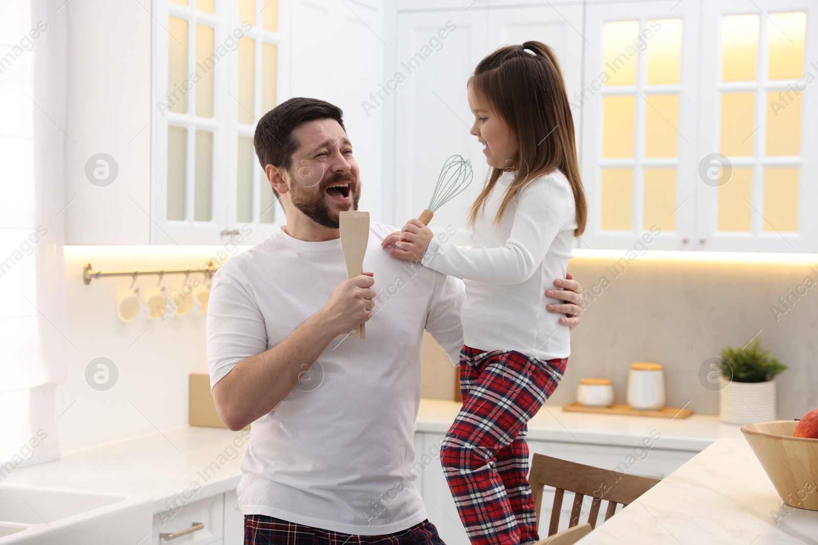 Photo of Father and his daughter wearing stylish pajamas having fun with cookware in kitchen