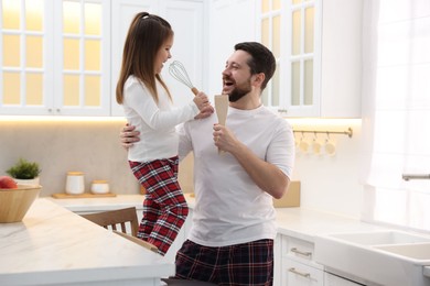 Photo of Father and his daughter wearing stylish pajamas having fun with cookware in kitchen