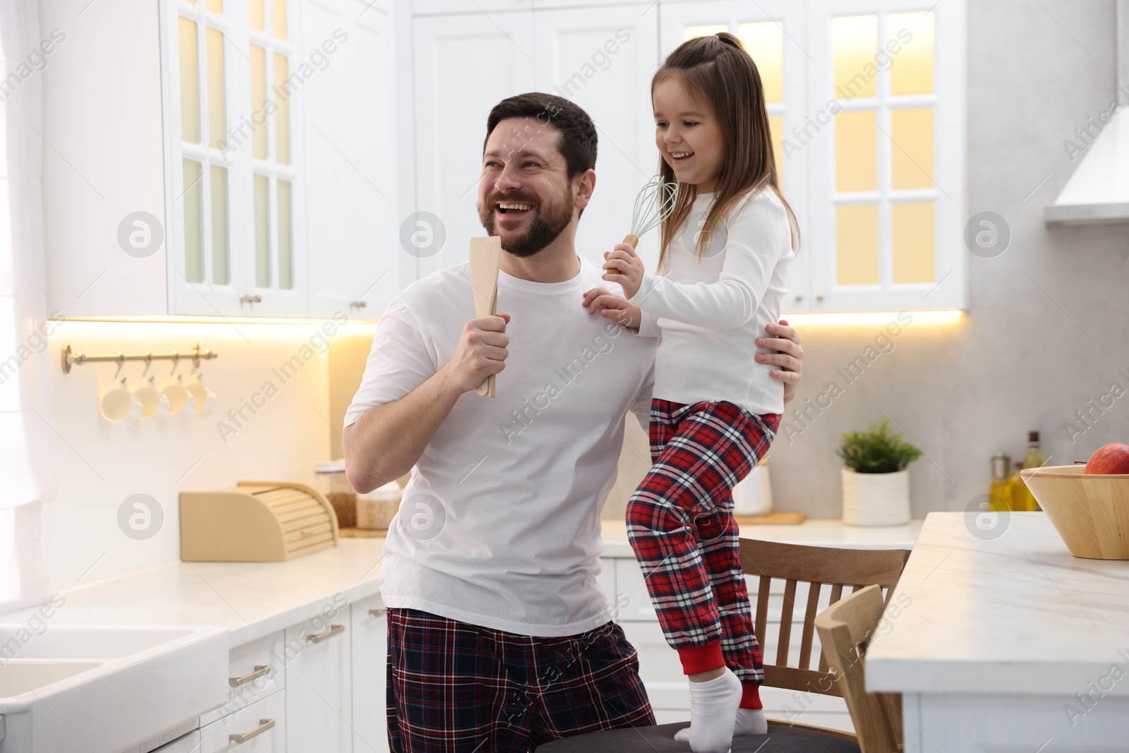 Photo of Father and his daughter wearing stylish pajamas having fun with cookware in kitchen