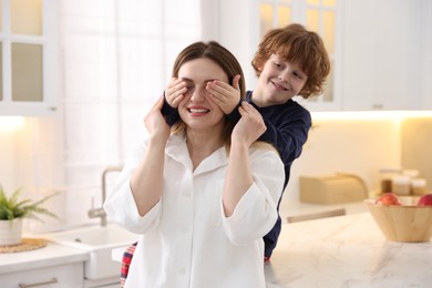 Photo of Smiling woman and her son wearing stylish pajamas having fun in kitchen