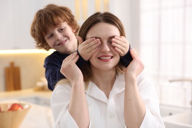 Photo of Smiling woman and her son wearing stylish pajamas having fun in kitchen