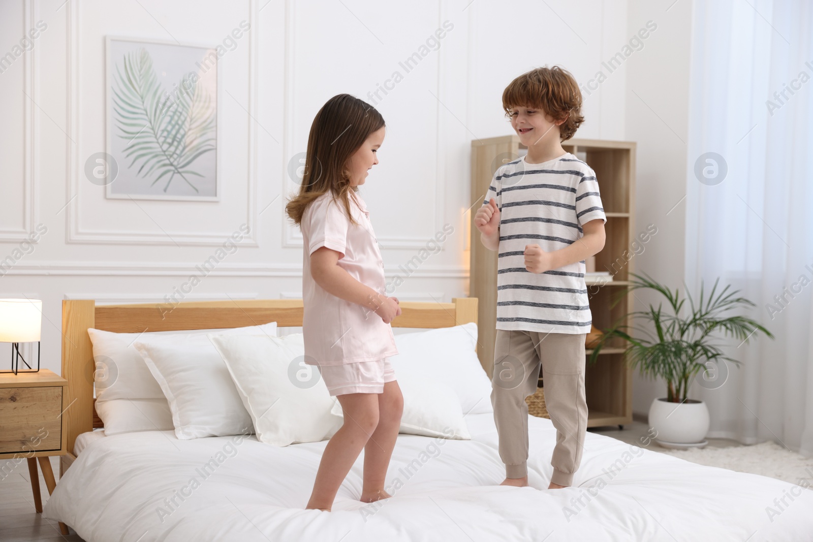 Photo of Children wearing stylish pajamas having fun on bed at home