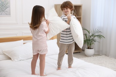 Photo of Happy children wearing pajamas having pillow fight on bed at home