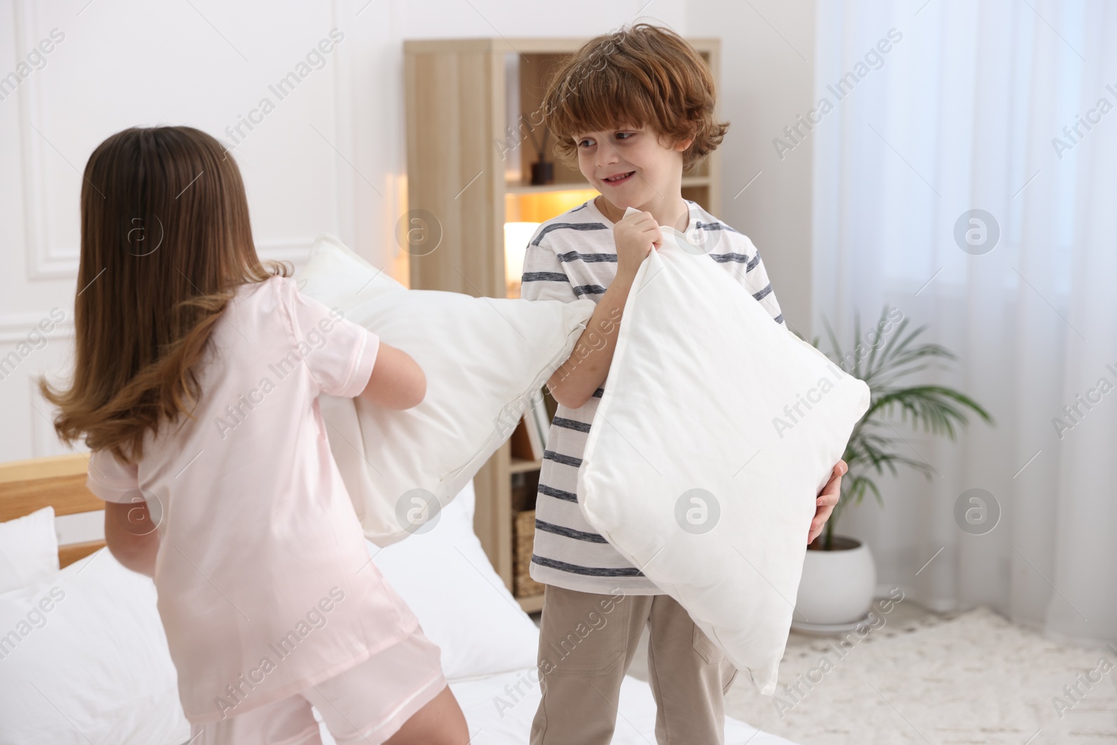 Photo of Happy children wearing pajamas having pillow fight in bedroom