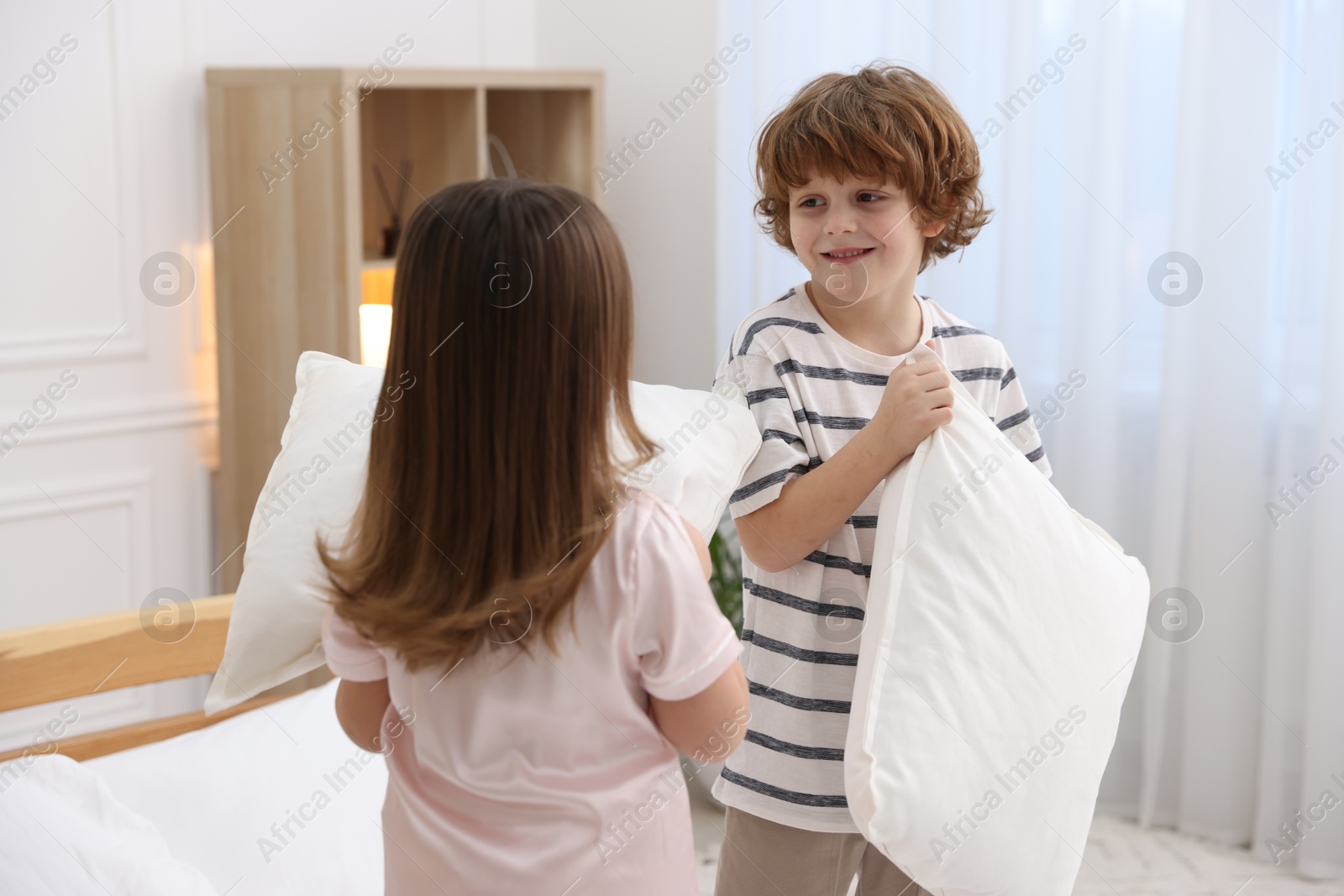 Photo of Happy children wearing pajamas having pillow fight in bedroom