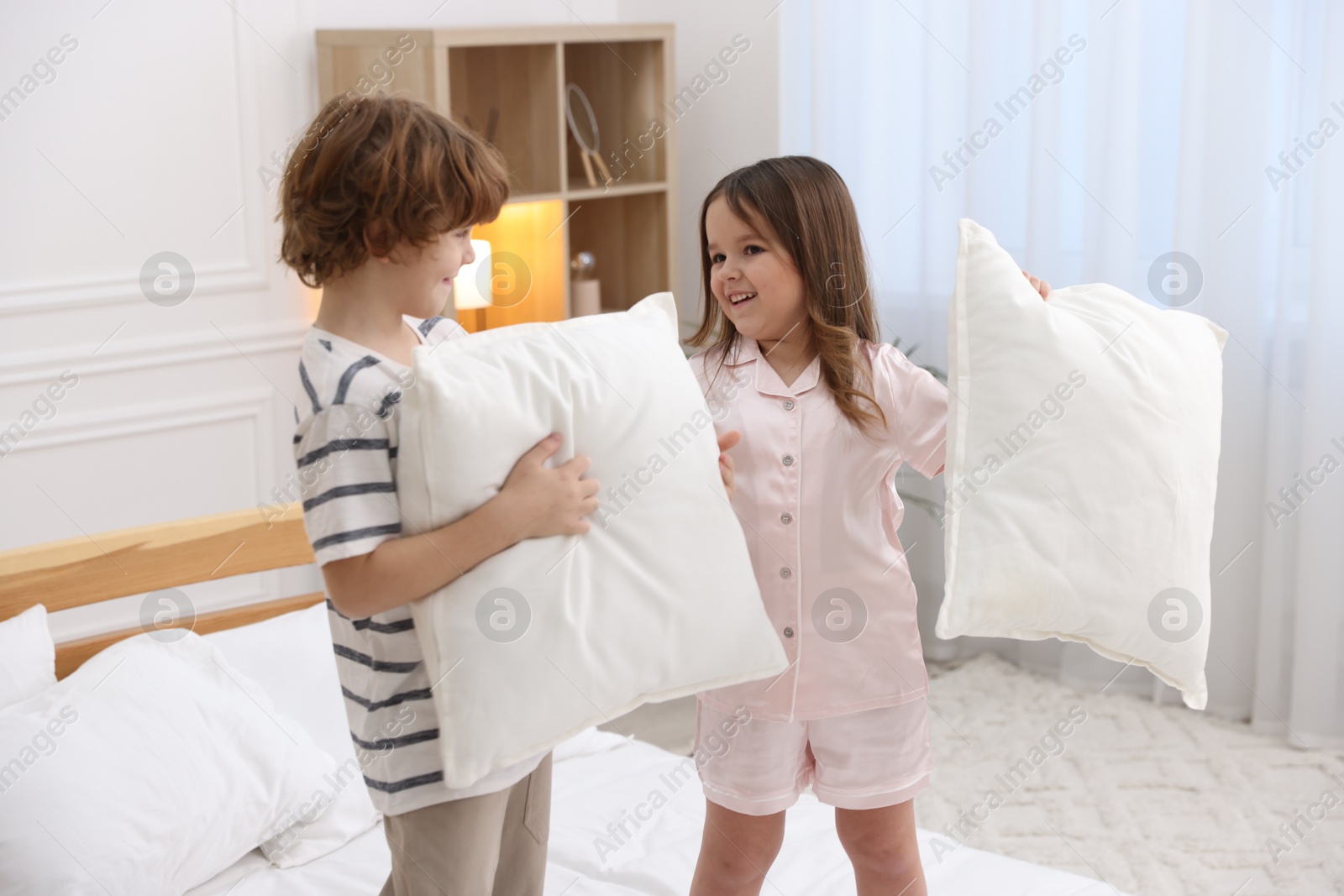 Photo of Happy children wearing pajamas having pillow fight on bed at home