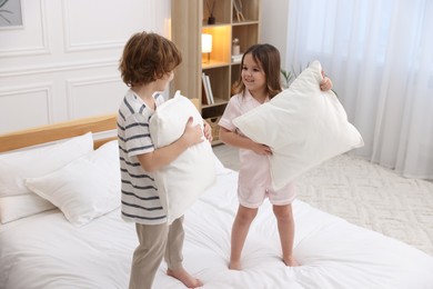 Photo of Happy children wearing pajamas having pillow fight on bed at home