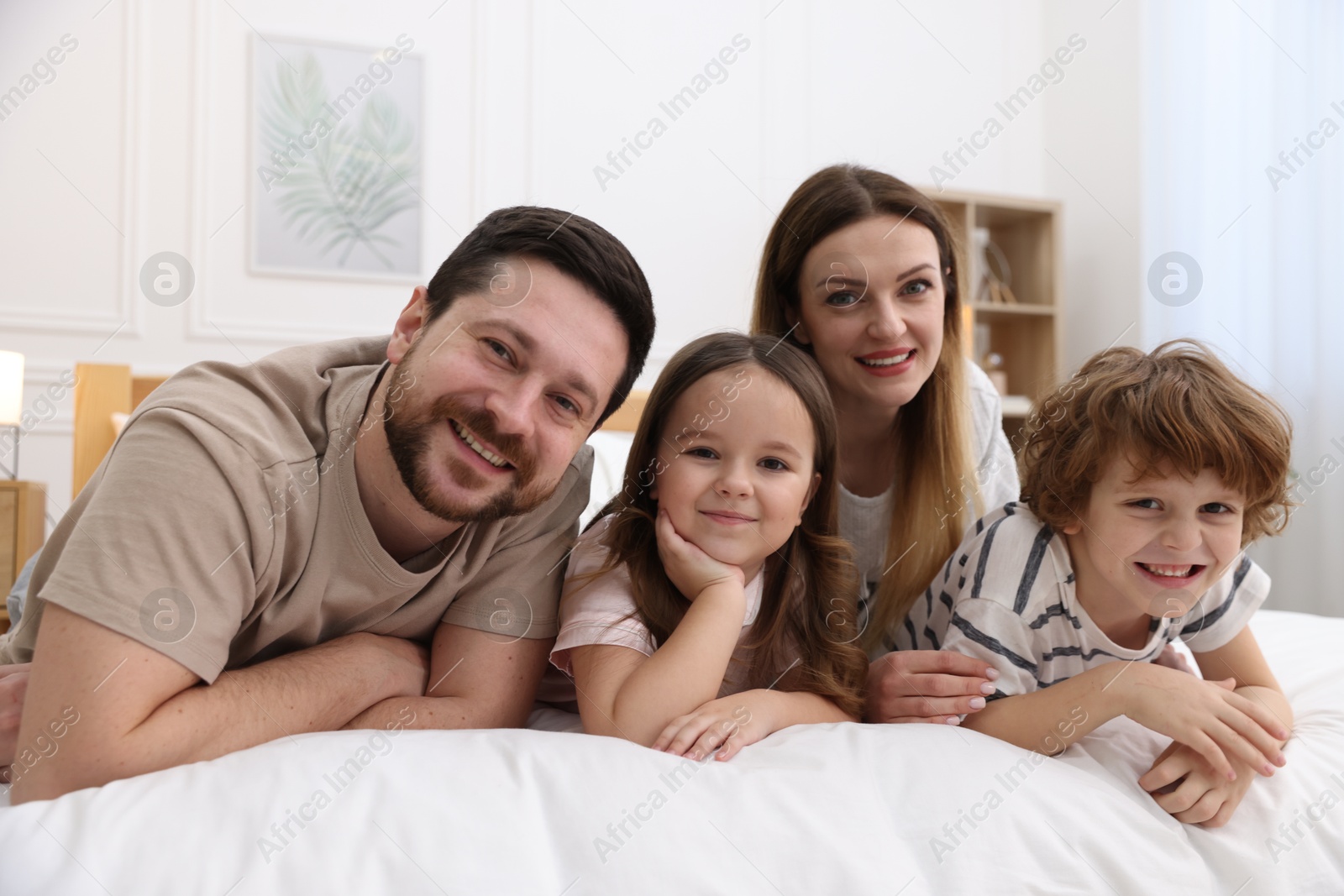 Photo of Family portrait of happy parents and their children wearing pajamas on bed at home