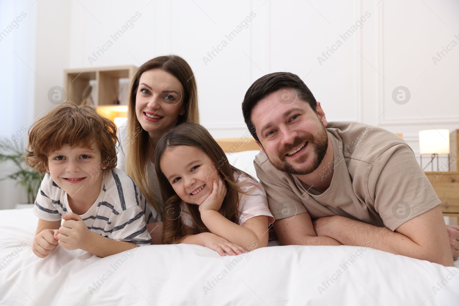 Photo of Family portrait of happy parents and their children wearing pajamas on bed at home