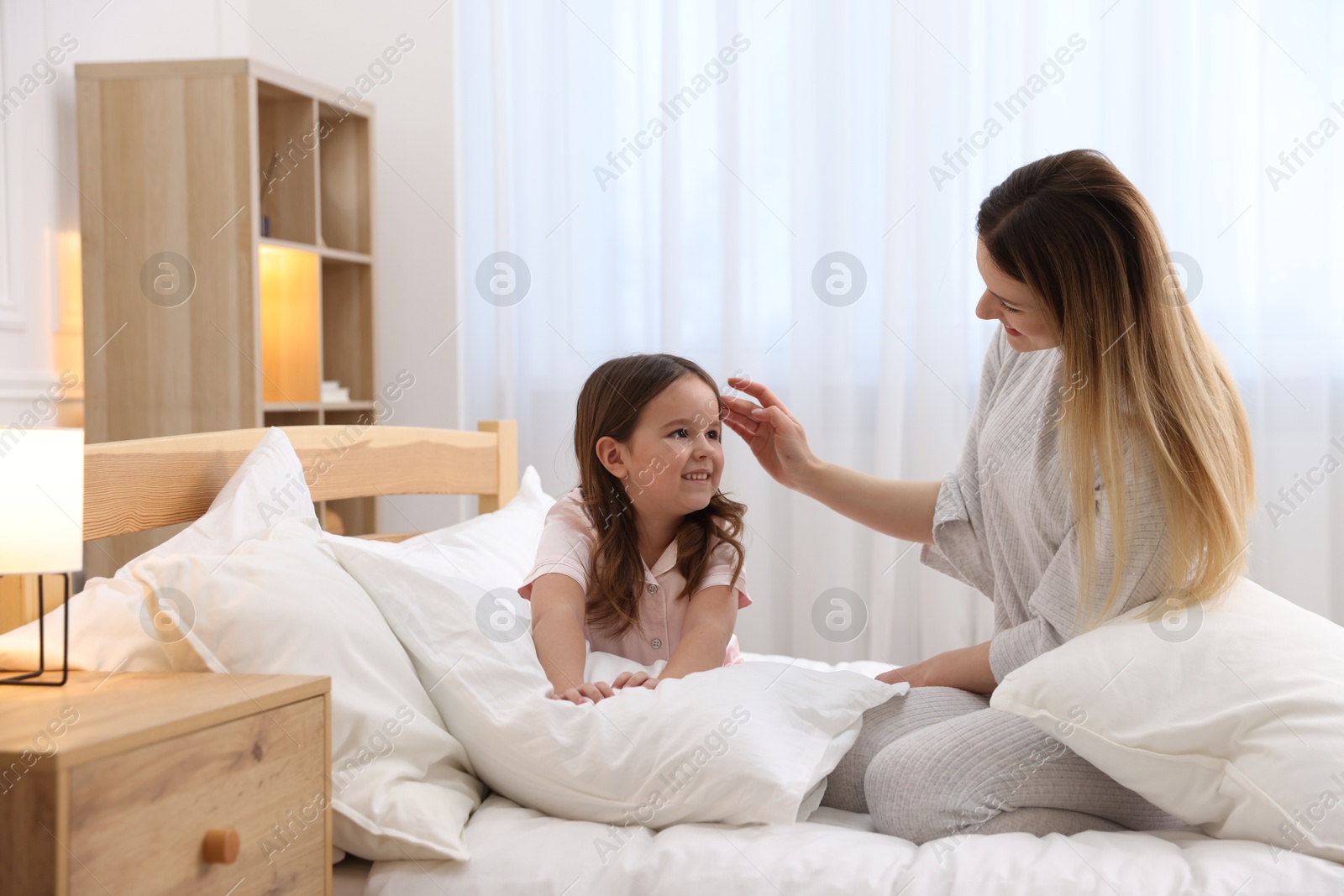 Photo of Happy mother and her daughter wearing pajamas on bed at home