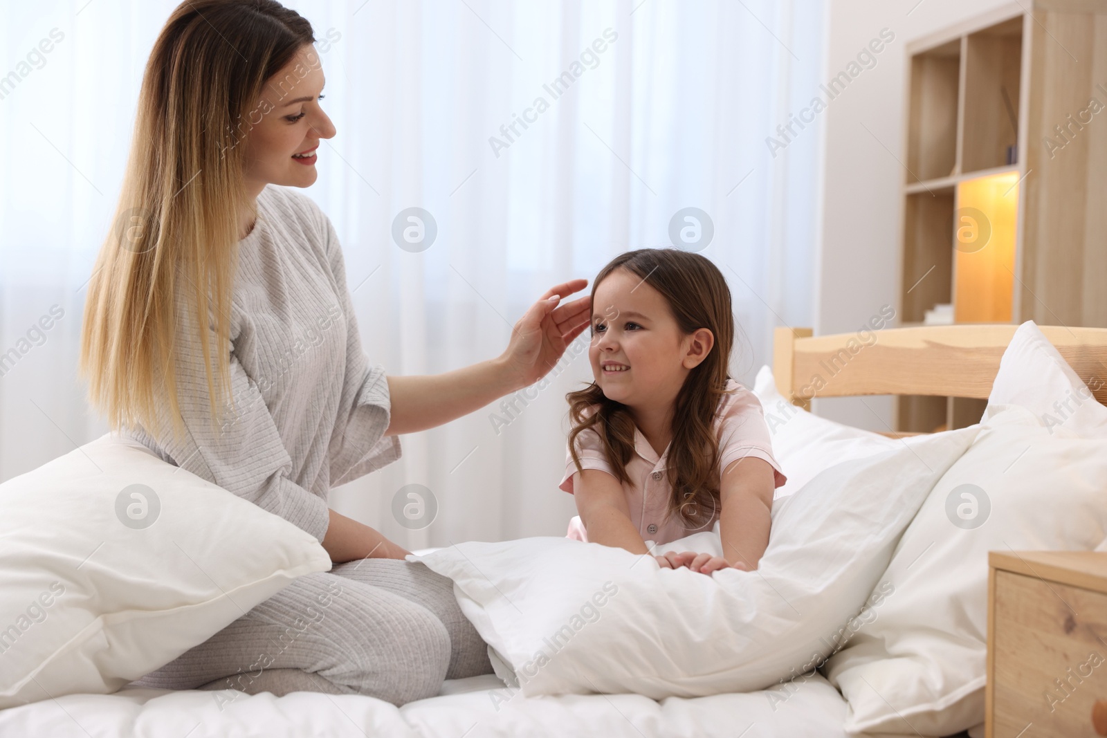 Photo of Happy mother and her daughter wearing pajamas on bed at home