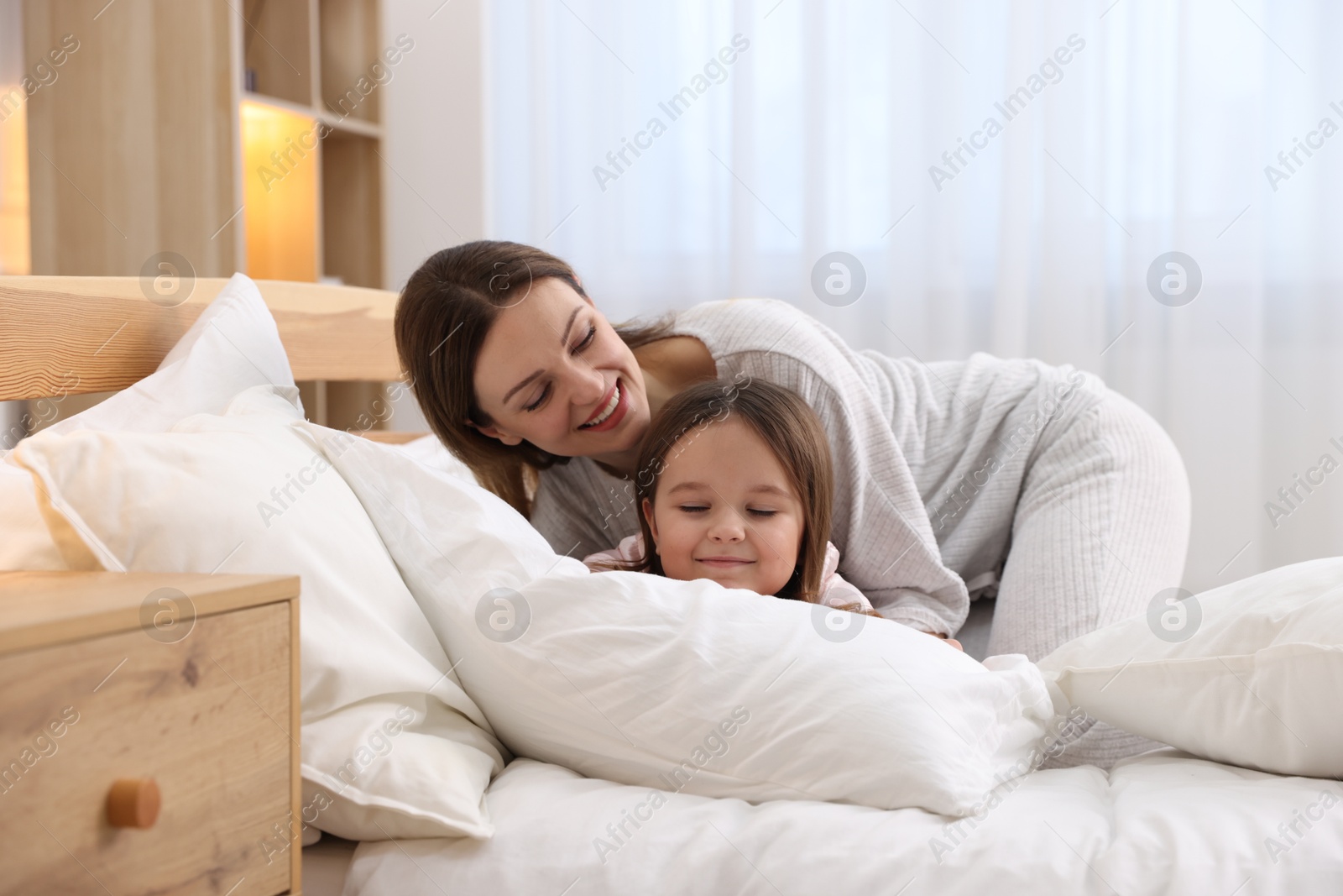 Photo of Happy mother and her daughter wearing pajamas on bed at home