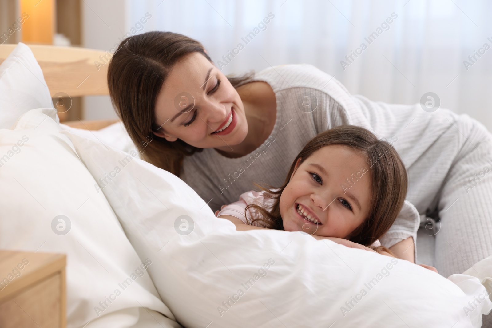 Photo of Happy mother and her daughter wearing pajamas on bed at home