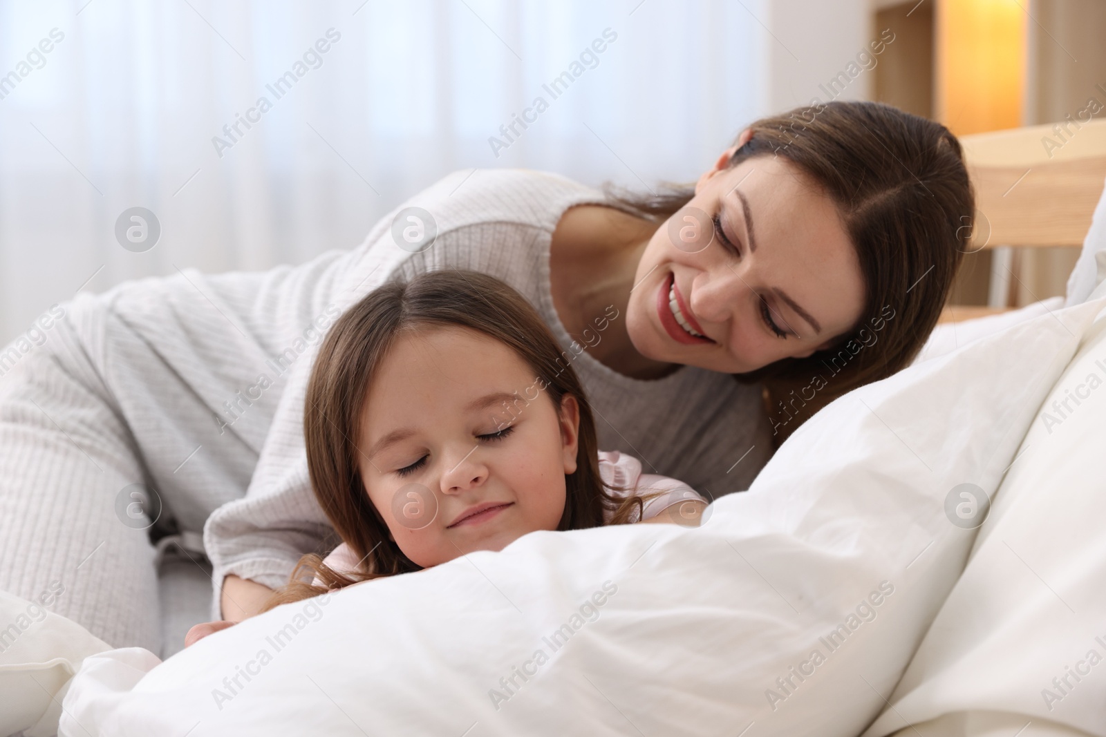 Photo of Happy mother and her daughter wearing pajamas on bed at home