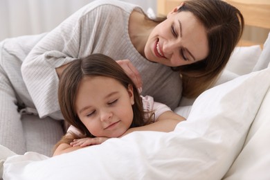 Photo of Happy mother and her daughter wearing pajamas on bed at home