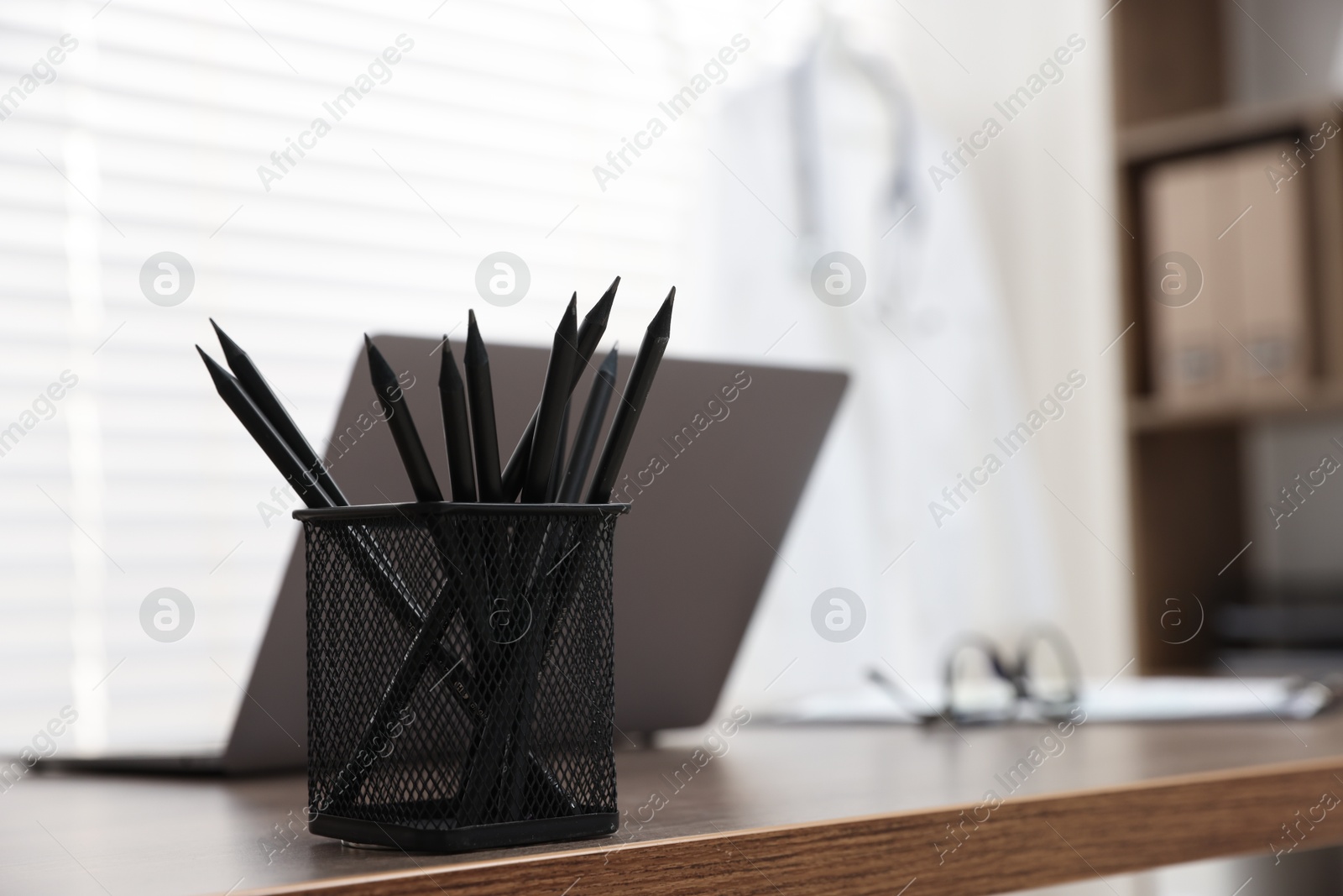 Photo of Laptop and holder with pencils on desk in medical office, closeup