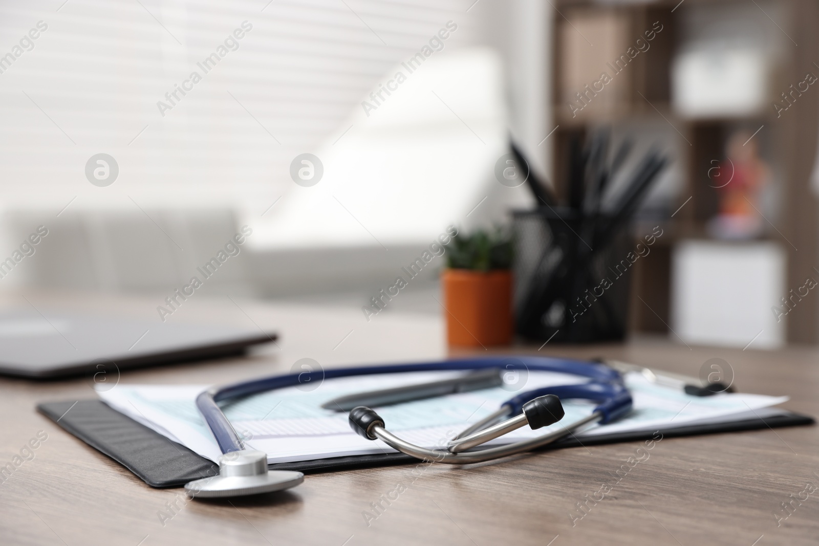 Photo of Clipboard and stethoscope on desk in medical office, closeup. Space for text