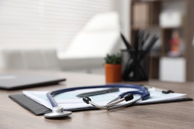 Photo of Clipboard and stethoscope on desk in medical office, closeup. Space for text