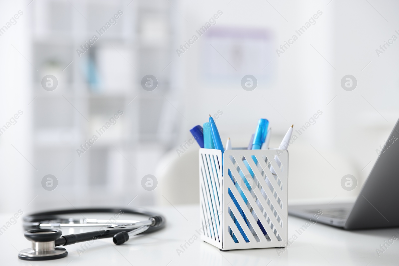 Photo of Laptop, stethoscope and holder with stationery on desk in medical office, closeup. Space for text