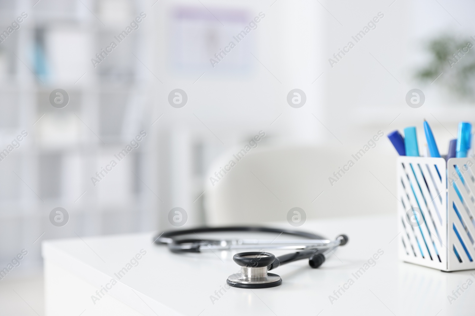 Photo of Stethoscope and holder with stationery on desk in medical office, closeup. Space for text