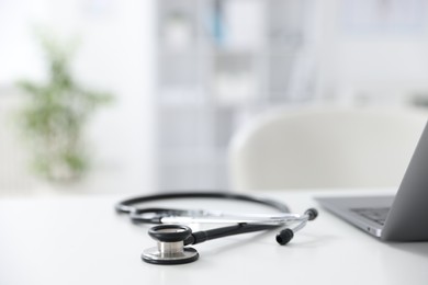 Photo of Laptop and stethoscope on desk in medical office, closeup. Space for text