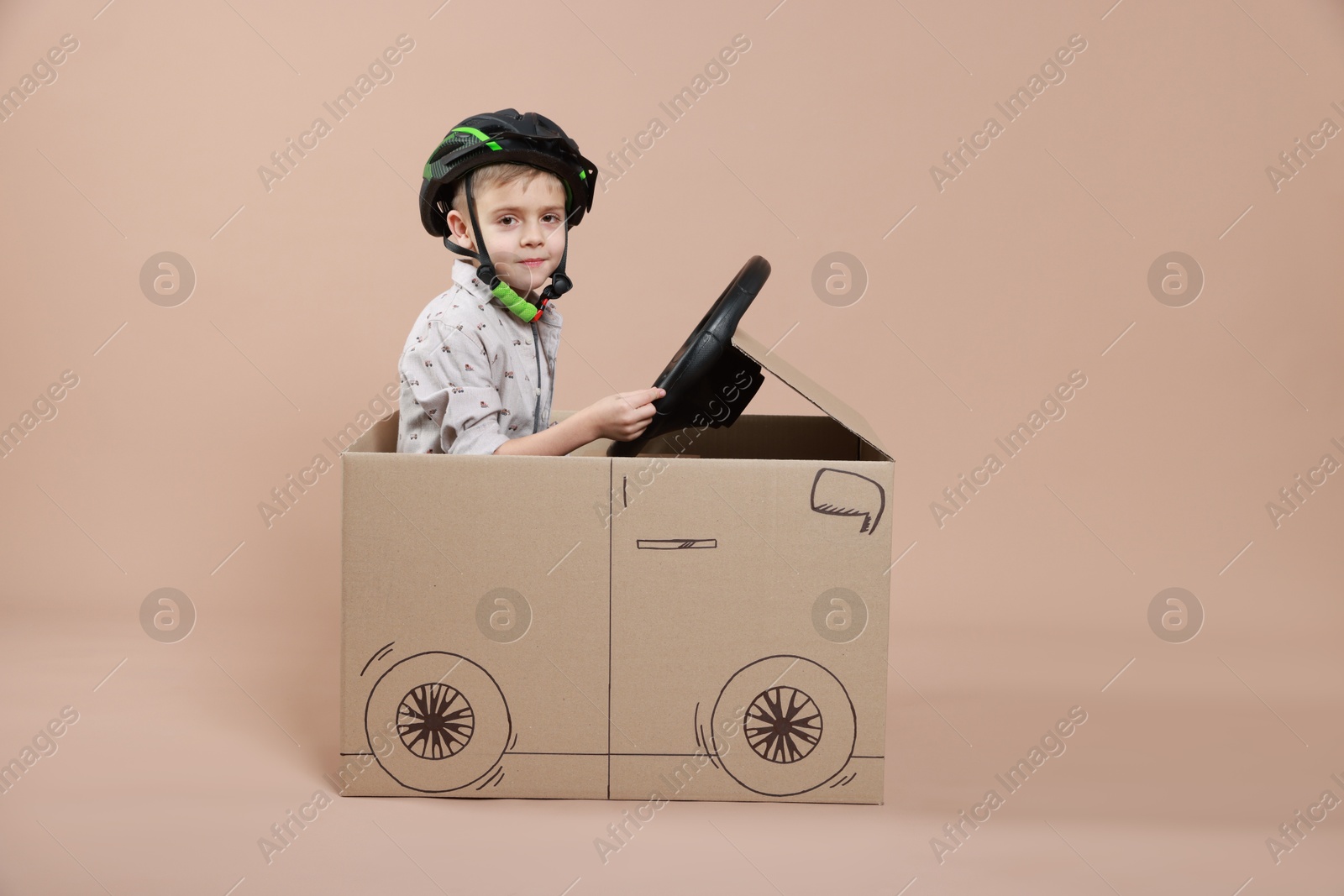 Photo of Little boy driving car made of cardboard on beige background